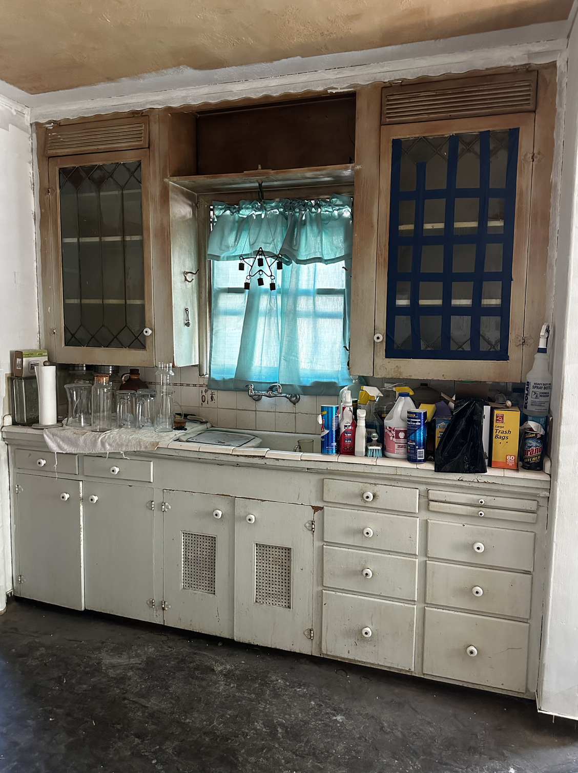 Current kitchen sink area with original cabinets, tile counter and window as it looks right now