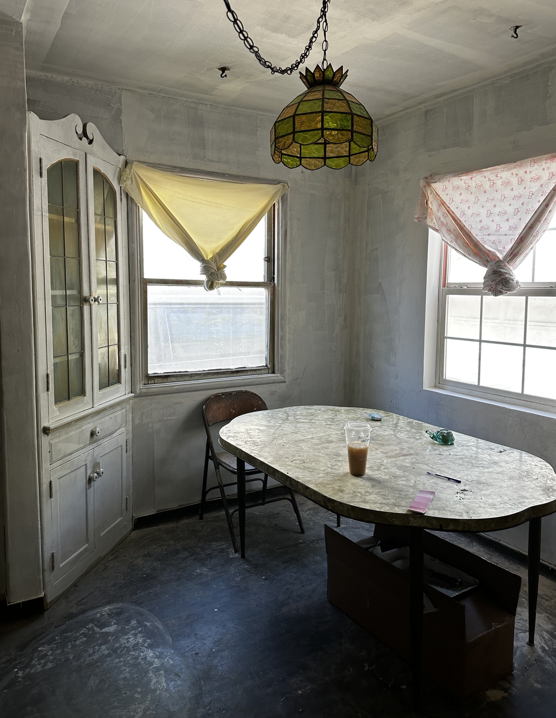 Current dining area with original built-in china hutch, bare plaster walls and concrete floor
